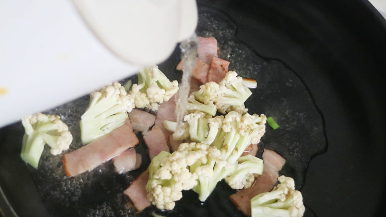 美味菜花炒培根,锅中倒入适量的开水,大火煮开5分钟后食物全熟即可盛盘。