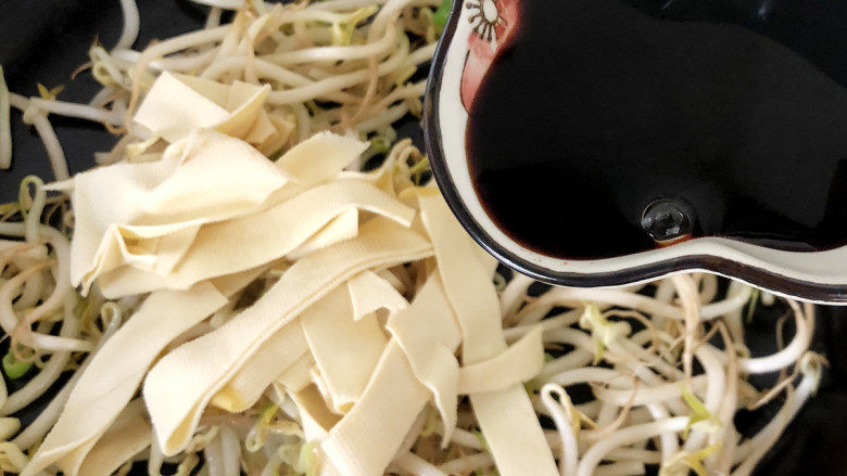 豆芽炒干豆腐,继续放入干豆腐翻炒均匀,加入适量的酱油进行调味。