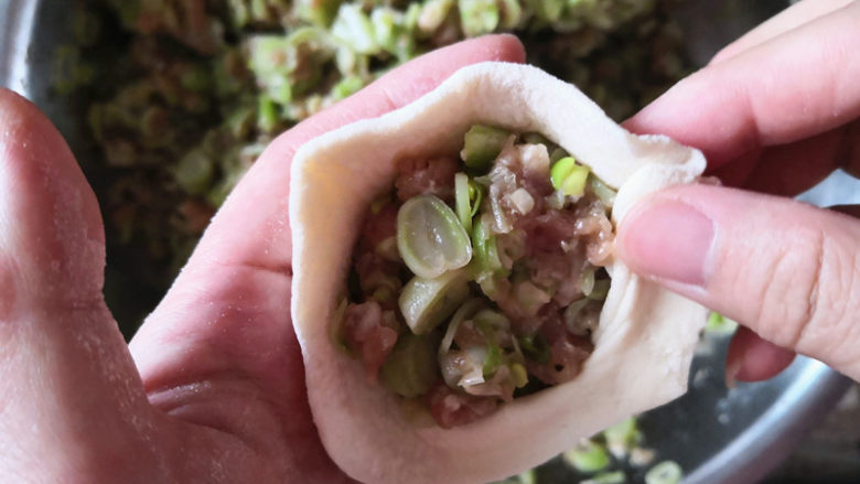 芸豆包子,把芸豆馅放到擀好的面皮里,左手托住,右手大拇指在上,食指捏着面皮边缘往前走,最后收口包好了,