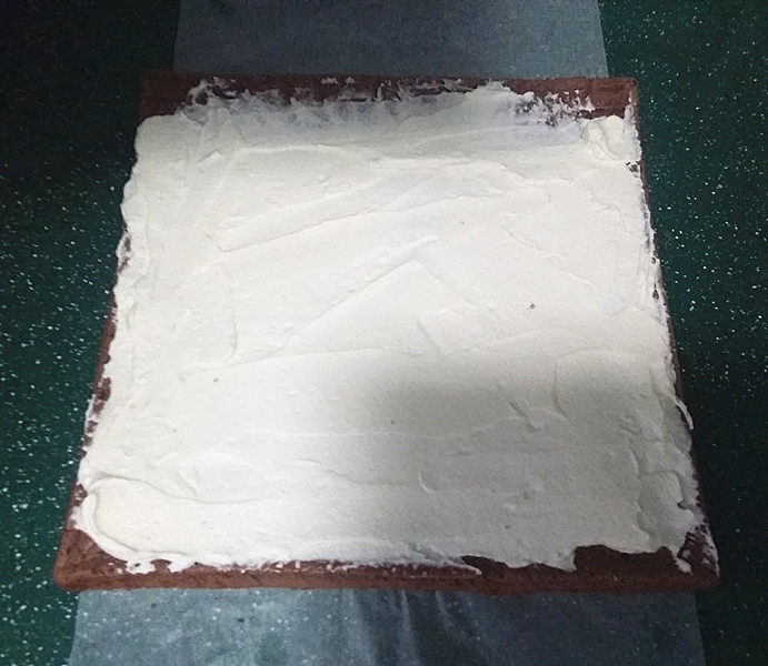 可可花奶油蛋糕卷,将蛋糕有花纹的那面铺在油纸上,然后将一半的奶油抹在蛋糕上、上面抹簿些、下端抹厚点