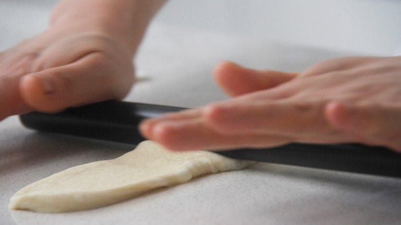 胖墩牛奶面包,取一份醒好的面团，擀成长条状后拍除周边汽泡，再翻面。