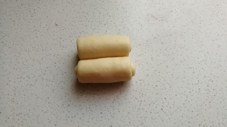 椰蓉炸面包,擀好后从两端向中间卷起,卷好后摆入烤盘。