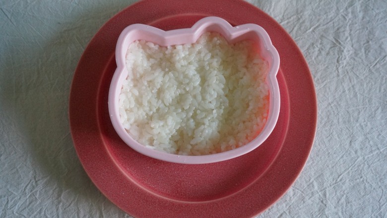 Kitty炼乳水果饭团,取一个盘子,把Kitty脸框放在盘子上,米饭填进去(这里剩一点米饭后面做Kitty的小爪)