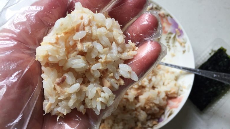 快手日式金枪鱼饭团,戴上一次性手套,取适量拌匀的米饭放在一手的掌心