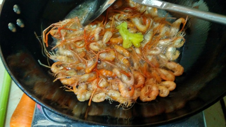 韭苔爆河虾,油热(开始冒烟)时,倒入控干水分的河虾和生姜,用锅铲轻轻翻搅均匀。