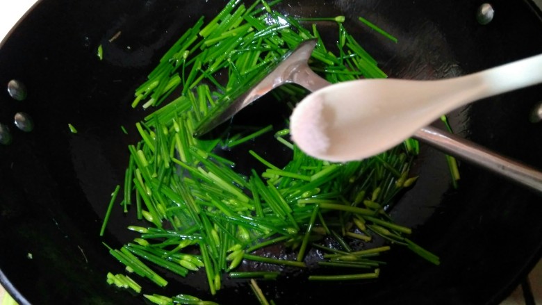 韭苔爆河虾,再次开火,锅中倒入少许虾油,油热后倒入韭苔,用手洒一些清水,加入一点点盐,翻炒至七分熟。