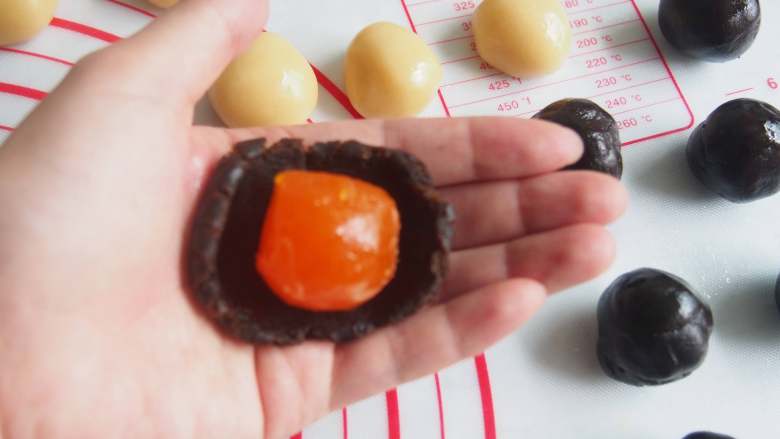 广式咸蛋黄豆沙月饼,将红豆馅压扁放入蛋黄包起来,再取面团在手心压扁,放入红豆蛋黄馅,用虎口轻轻收口。