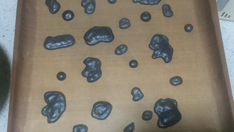 奶牛蛋糕卷,此时,我们将烤箱提前预热。烤盘中铺好油布,黑色蛋糕糊装入裱花袋中,在油布上随意挤出奶牛的花纹状。
用180度烤2分钟后取出