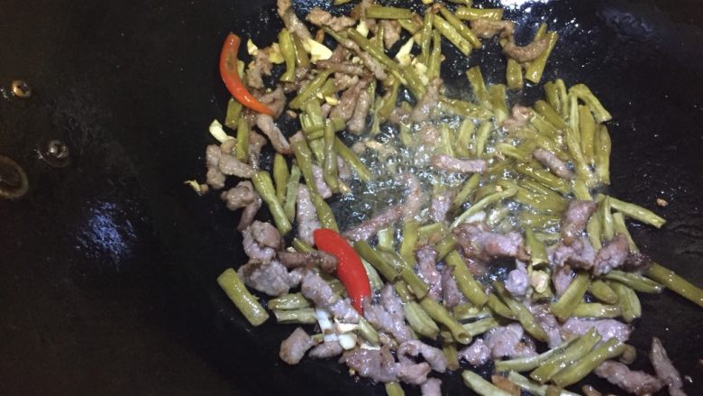 辣炒牛肉酸豆角,锅中倒入油，烧热后依次放入牛肉、酸姜碎和酸豆角，适当翻炒。