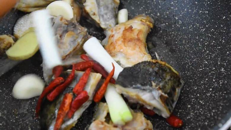 鲜香不腻,味道实在太好吃的红烧三文鱼头煲,热锅冷油,放入鱼头,煎至微焦。
再倒入葱、姜、蒜、干辣椒,炒匀。