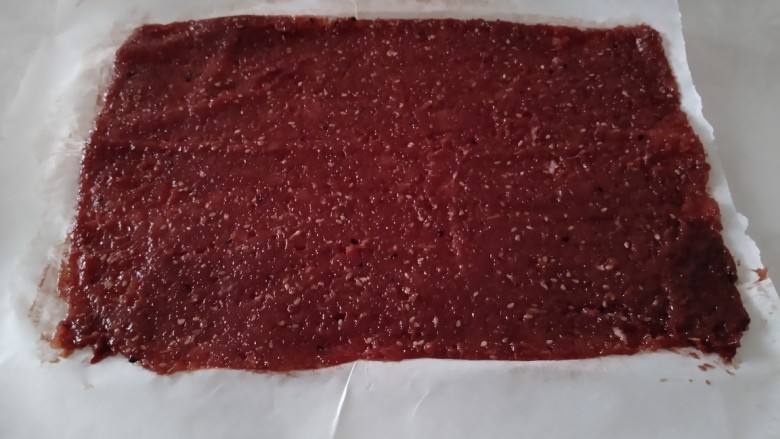 蜜汁猪肉脯,铺在油纸上,上面也铺一张油纸,慢慢的擀成0.3厘米厚,借助刮板整形后,拿掉上面的油纸。