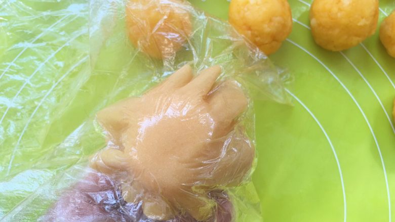 爱心金沙月饼,之后揭掉一层保鲜膜,包裹上金沙馅,再揭掉下层保鲜膜,用虎口部分一点点推揉面团,将金沙馅包裹上;
