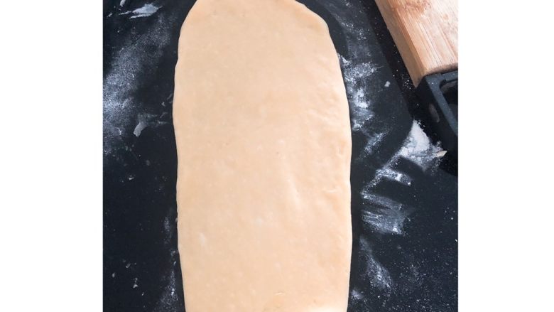 葱香火腿腊肠肉松面包,将面团揉成6个小面团,用擀面杖擀成如图示的长面饼。(擀面饼时面板需撒一层薄面粉,否则面饼会粘在面板不易取出)