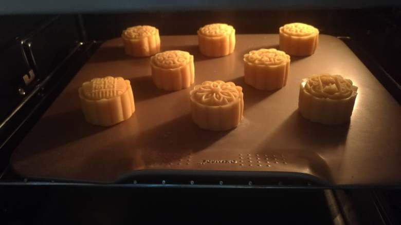 流心金沙奶黄月饼,烤箱中层,上下火180度,烤5分钟定型,取出烤盘,表面刷上一层蛋黄液(刷子先在碗边刮一下再刷,只用薄薄一层)再放回烤箱,烤8分钟左右(时间和温度请结合自己烤箱实际,注意观察上色情况,烤太久流心容易爆出来)