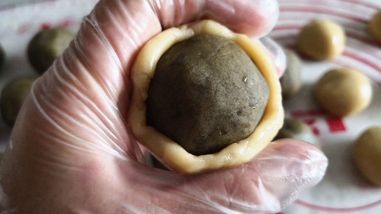 绿豆沙蜜豆月饼,月饼皮用手按扁,中间包上揉好的绿豆沙蜜豆球,面皮比较软,所以要慢慢轻轻地用虎口往上推面皮,将其内馅包住,