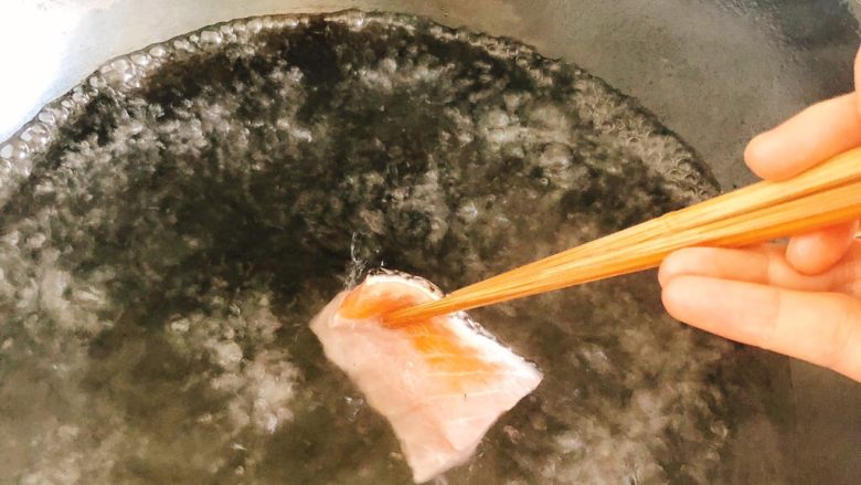 白灼沙拉三文鱼-西餐、年夜饭,锅里烧开水,用筷子夹着三文鱼片逐片放入水中。
