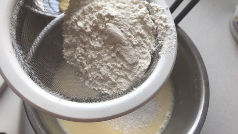 芒果盒子蛋糕,把面粉过筛到鸡蛋牛奶打好的液体中,搅拌至顺滑无颗粒状态。