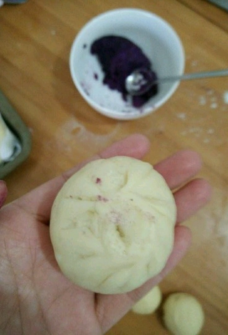 圣诞小娃娃,取个大的剂子,放适量紫薯陷,包好并搓成椭圆形。(稍微搓一下,比圆形长一点就好。)然后摆在烤盘里,再取个小剂子搓圆,抹点水,沾到椭圆形包子上方。