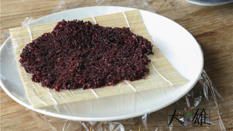 回忆杀,自制咸蛋黄肉松紫米饭团子,准备好一个大的盘子或者在砧板上操作,先放上寿司帘,再铺上一层保鲜膜,保鲜膜的长度要够长这样才能保证米饭不会漏出来