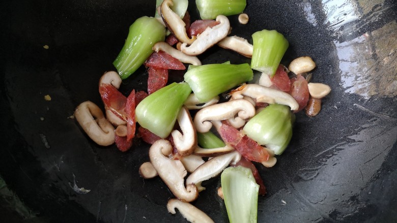风味炒拉条子,锅中再加入适量的油烧热后下入腊肠,香菇和青菜梗先翻炒一下,至青菜梗变色。