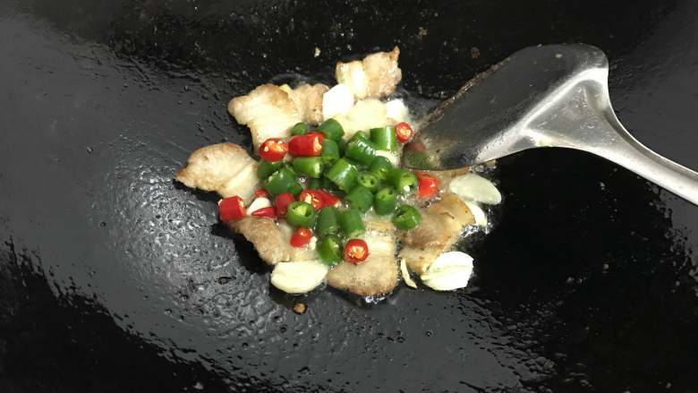 麻辣干锅土豆,锅中倒少许油,下五花肉煸炒。
放入蒜片和青、红椒,炒出香味。