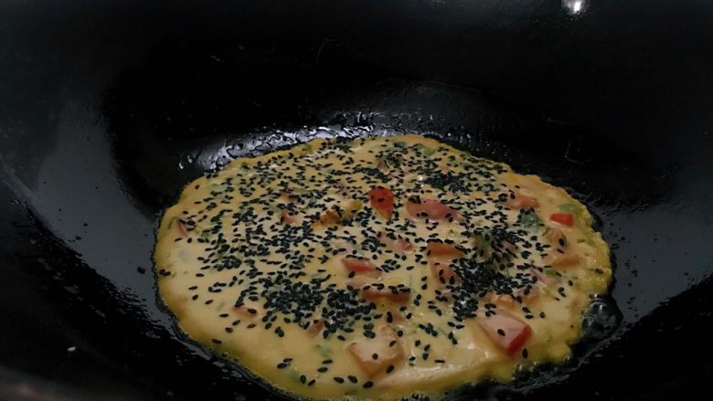 十味 番茄鸡蛋饼,热锅中加入适量油,倒入面糊,上面撒<a style='color:red;display:inline-block;' href='/shicai/ 668'>黑芝麻</a>,表面凝固,底煎金黄后翻面。