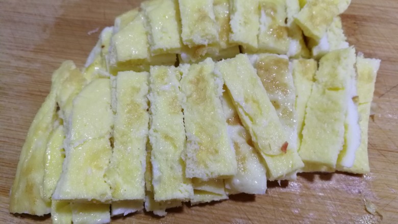 牛肉蒜薹炒蛋条,煎熟的蛋饼放在案板上,用刀切成小条,如图↑