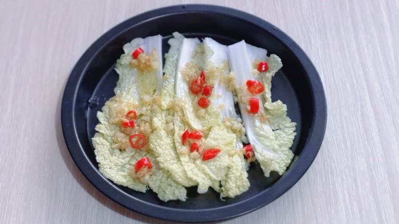 15分钟get惊艳大餐~烤海鲜,将洗干净的娃娃菜切条,铺在烤盘底下,把腌制虾的酱汁淋在娃娃菜上,再盛一勺辣椒蒜末油浇在上面。