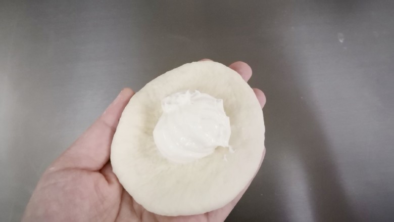 奶酪早餐包,取一个醒发好的面团压扁排气,包上奶酪馅。