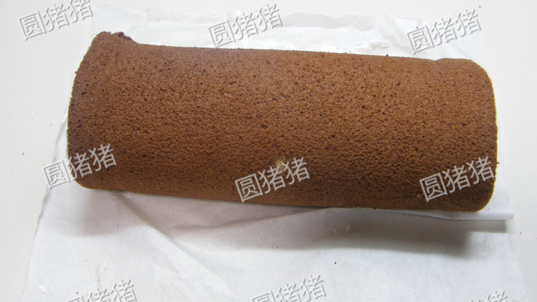 可可奶冻卷,底垫蛋糕纸,用擀面棍辅助将蛋糕卷起,并包住放入冰箱冷藏30分钟定形。