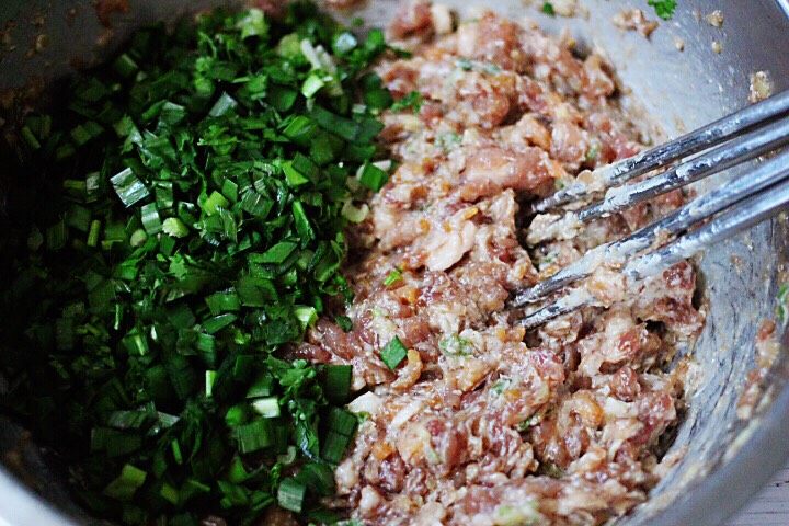 胶东半岛的三鲜馄饨,用筷子搅拌均匀所有的食材后,放入切碎的<a style='color:red;display:inline-block;' href='/shicai/ 116'>韭菜</a>。