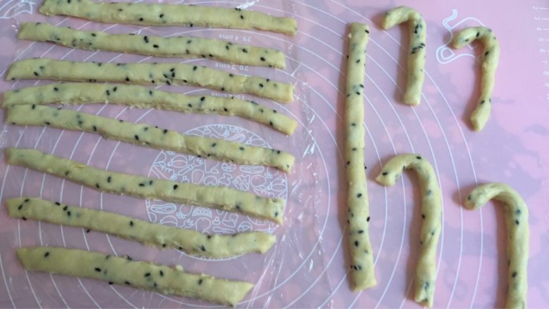 芝麻奶油拐棍饼干,切条,再将其捏成拐棍造型,摆入烤盘;