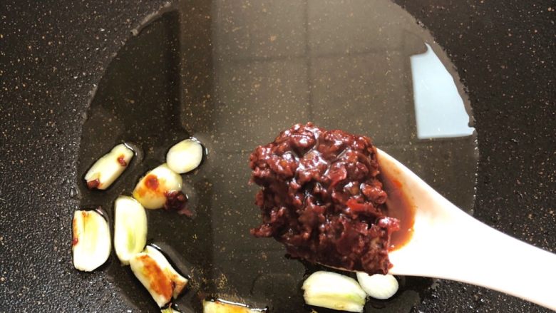 鱼香杏鲍菇,锅中放油烧热,蒜瓣放进去加1汤匙红油豆瓣酱翻炒出红油