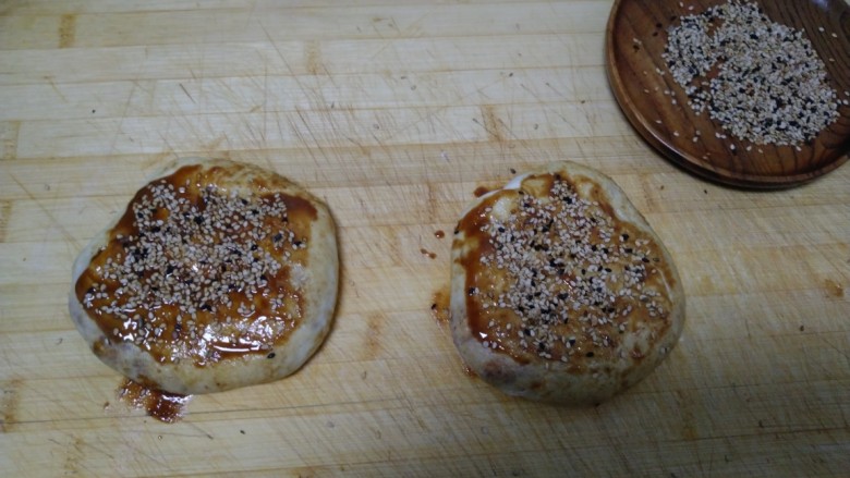 芝麻酱烧饼,卷起来平均分成2份,收紧口,用手按扁,表皮再均匀涂上芝麻酱,撒上芝麻,用手压一压。