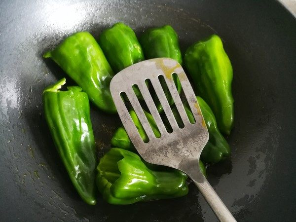 虎皮青椒,锅中倒入油烧六成热,放入青椒分散开,不要翻动,用锅铲按压青椒,改小火油煎。