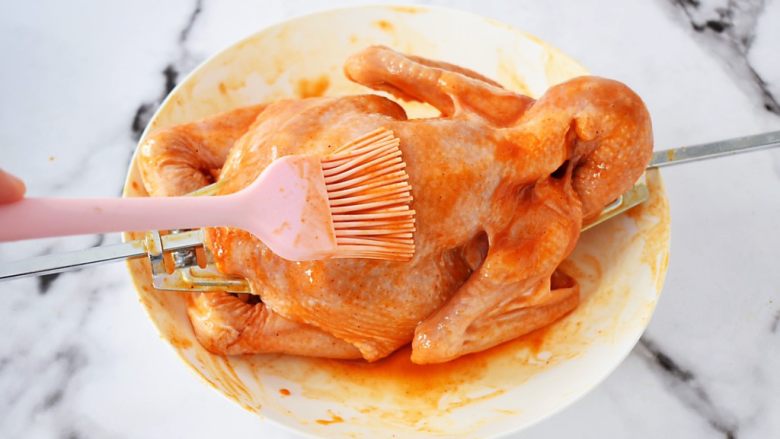 奥尔良烤全鸡,把煮沸的蜜汁腌料先在三黄鸡全身涂抹一遍,不要全涂完,留下一点,因等下还要再刷一遍,这样能让鸡烤出来颜色更漂亮