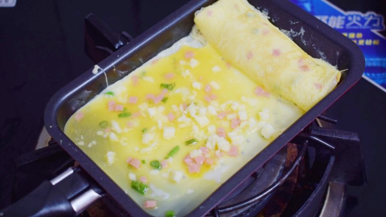 芝士火腿厚蛋烧,再舀进1大勺鸡蛋液,再撒上芝士碎,小火煎至底部凝固