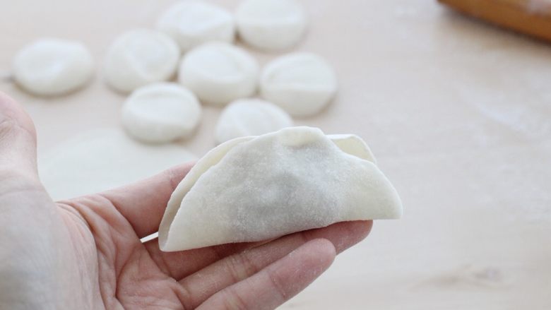 猪肉莲藕馅饺子,取一个饺子皮用左手托住,在饺子皮上放适量的馅料,将饺子皮中间对折捏严