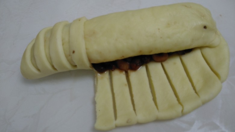 百香果奶味🐛豆沙面包,从有豆沙的这边开始卷起，把有都豆沙的地方全部卷上，把没有卷的那边用刀切成一条一条的。