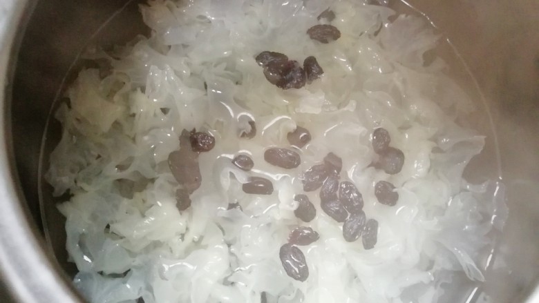 百变水果 苹果香橙银耳羹,砂锅内放水烧开,下入银耳和葡萄干再次烧开,转中小火煮40分钟。