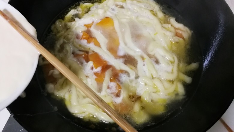 蒜香南瓜面疙瘩,筷子压着碗边的面团,压出比筷子细一点面条,将面条拨下锅,烧开转小火烧一分钟
