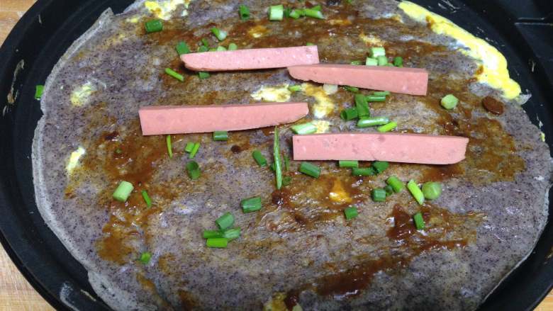 紫米面煎饼果子,再翻面涂上酱,撒上香葱、放上香肠(喜欢辣的可以涂点辣酱)