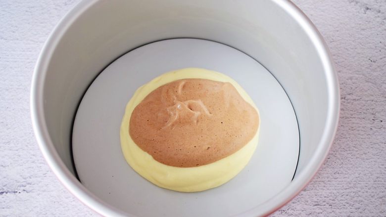 斑马纹戚风蛋糕,先用汤勺舀一勺原味蛋糕糊从中间滴落入模具中,再用另一个汤勺舀一勺可可蛋糕糊从原味面糊中间滴落下来