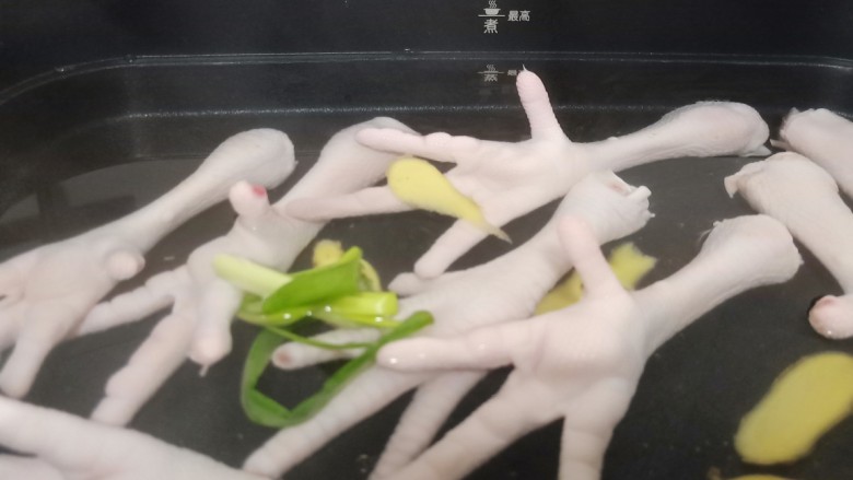 下酒小菜《香辣红烧鸡爪》,锅里加适量的清水(加水位置不能超过煮食物的最高位)冷水下鸡爪、加点生姜片、葱一起煮。