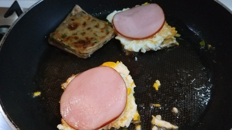 新文美食 葱油饼沾鸡蛋加肠片,把火腿片放在鸡蛋上。在盖上一块葱油饼