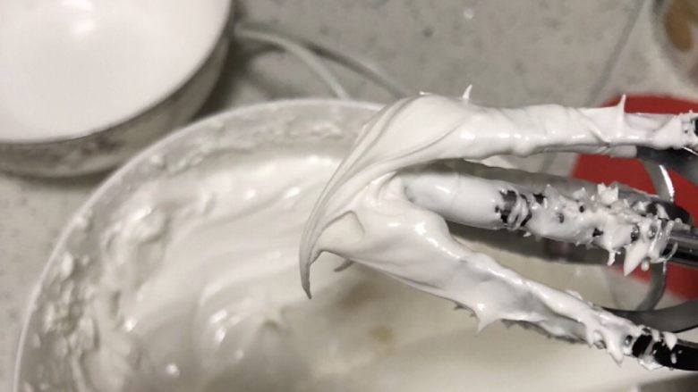 圣诞小屋,用打蛋器高速打发。第一次打到一般的硬度，如图，没有直直的尖锋。因为考虑到我用的大部分蛋白霜不需要太硬。取出一部分，加入色素调好颜色。剩余的蛋白霜继续打发，打成硬糖霜状态。硬糖霜适合粘合拉线印花，后面要用到粘合屋子。一般硬度的糖霜适合裱饼干的轮廓和花卉，较软的糖霜适合饼干填充。
打好的糖霜如果需要更软，可适当加水进去，如果需要更硬可适当加入糖粉。