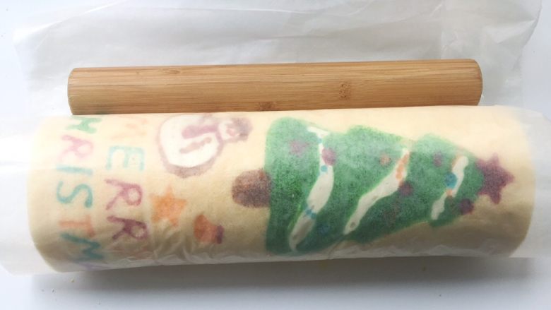 圣诞树蛋糕卷,之后借用擀面杖的力度,将蛋糕卷卷起来,卷好后,用擀面杖压一下油纸轻轻收紧,定下形