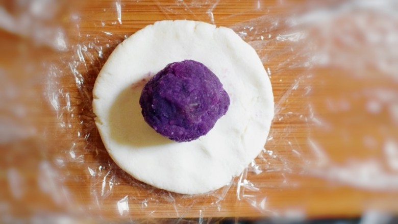 紫薯山药糯米饼(微笑饼),取一个剂子,用手压成饼状,并取一个紫薯泥团子,放在饼上。