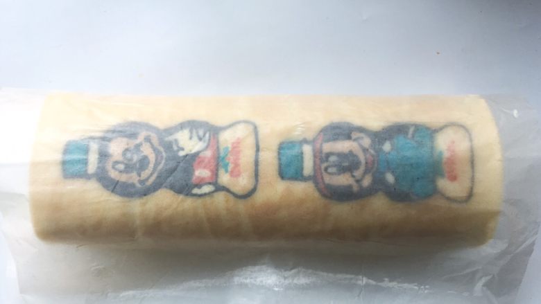 依云米奇蛋糕卷,用擀面杖卷起底下的油纸,利用擀面杖将蛋糕卷卷起来,之后用擀面杖将油纸收紧,给蛋糕卷定形