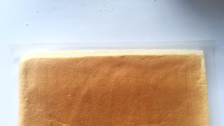 依云米奇蛋糕卷,蛋糕卷下铺油纸,用锯齿刀斜着裁掉一侧的边缘,裁的时候看一下米奇的位置,别裁错边啦